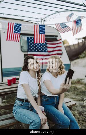 Eine schöne Aufnahme von zwei spanischen Frauen, die ein Selfie machen Auf dem Hintergrund der US-Flaggen - Tag der US-Unabhängigkeit Stockfoto