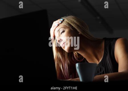 Erschöpfte Geschäftsfrau, die in einem dunklen Büro Überstunden machte und sie ruhte Kopf auf der Hand mit geschlossenen Augen, während sie nimmt Ein Moment zum Entspannen Stockfoto