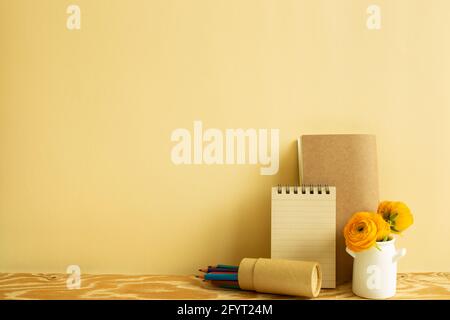 Notizbuch, Buntstifte, Blume auf Holzschreibtisch. Beiger Hintergrund. Arbeits- und Studienort Stockfoto
