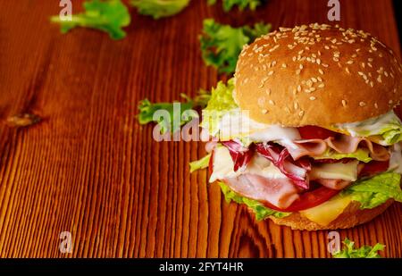 Burger mit Salat, Käse, Schinken und Tomaten auf dunklem Hintergrund. Nahaufnahme. Stockfoto