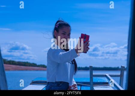 Eine junge Frau mit gemischter Rasse (1/2 Khmer und 1/2 kambodschanische Hügelstämme) macht während einer Bootsfahrt auf dem West Baray Reservoir ein Selfie. Aufgrund der niedrigen Fallzahl von COVID in Kambodscha - 19, glauben viele Kambodschaner, dass sie während der Coronavirus-Pandemie keine Gesichtsmasken tragen müssen. Archäologischer Park Angkor, Provinz Siem Reap, Kambodscha. Mai 2020. © Kraig Lieb Stockfoto