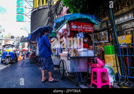 Ein Mann, der einen blauen Regenschirm hält, wartet darauf, von einem Food-Cart in Chinatown, Bangkok, Thailand, Essen serviert zu bekommen Stockfoto