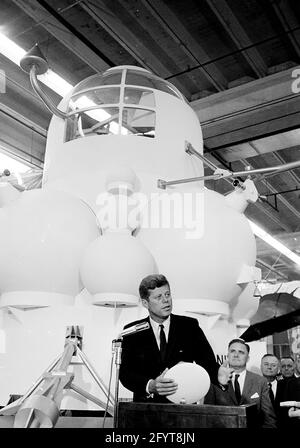 12. September 1962Präsident John F. Kennedy (auf dem Rednerpult) gibt nach einer Führung durch Raumfahrzeuge in einem Hangar im Rich Building des bemannten Raumschiffszentrums, Houston, Texas, eine Rede ab. Präsident Kennedy hält ein maßstabsgetreues Modell des Apollo-Kommandomoduls, das ihm der Direktor des bemannten Raumschiffszentrums, Dr. Robert Gilruth, präsentiert hat; im Hintergrund sitzt ein Modell des Mondlanders (auch bekannt als „der Bug“). Im Hintergrund: Administrator der National Aeronautics and Space Administration (NASA), Dr. James E. Webb; Gouverneur von Texas, Price Daniel; Stockfoto