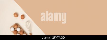 Banner mit Eiern in Holzeierkasten und Schneebesen auf beigem Hintergrund. Flach liegend Draufsicht Kopierbereich. Stockfoto