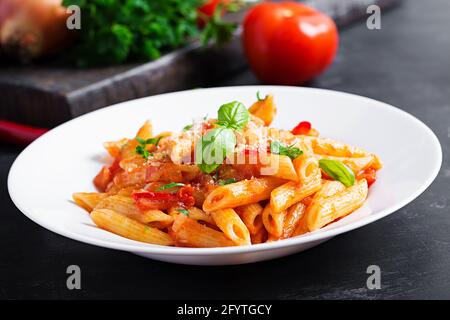 Klassische italienische Pasta Penne alla arrabiata mit Basilikum und frisch geriebenem Parmesankäse auf dunklem Tisch. Penne mit Chilisauce arrabbiata. Stockfoto