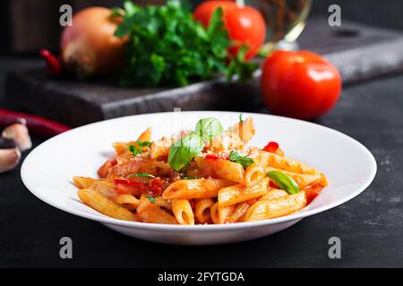 Klassische italienische Pasta Penne alla arrabiata mit Basilikum und frisch geriebenem Parmesankäse auf dunklem Tisch. Penne mit Chilisauce arrabbiata. Stockfoto