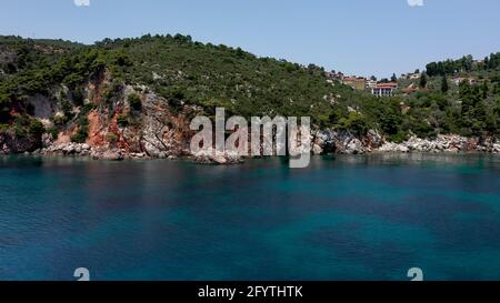 Luftdrohnen-Ansichten über eine felsige Küste, kristallklares ägäisches Meer, touristische Strände und viel Grün an einem wolkenlosen Tag in Skopelos isla Stockfoto