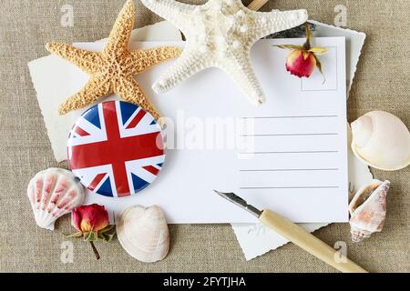 Postkarte mit Platz für Ihre Grüße, Muscheln um. Die Flagge von Großbritannien, allgemein bekannt als Union Jack auf Knopf Abzeichen gedruckt. Stockfoto