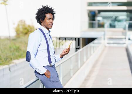 Schwarzer Mann mit Afro-Frisur mit einem Smartphone in der Nähe eines Bürogebäudes. Stockfoto