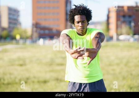 Schwarzer Mann mit Afro-Haaren, der sich nach dem Laufen im Freien dehnt. Stockfoto