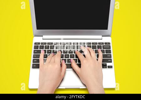 Draufsicht Bild von perfekten weiblichen Händen tippen auf ein Laptop auf gelbem Hintergrund Stockfoto