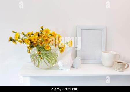 Ein Bouquet von Delelionen in einer weißen, geriffelten Vase und zwei Tassen in verschiedenen Größen mit Kaffee auf einem weißen Tisch. Frühstück. Speicherplatz kopieren Stockfoto