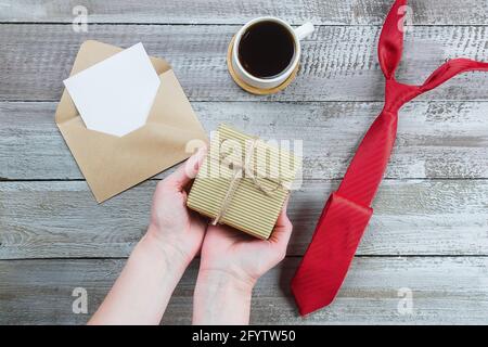 Alles gute zum Vatertag. Frau Hände halten Geschenk oder Geschenkbox. Rote Krawatte, Tasse Kaffee und leere leere leere Gcard auf Holzhintergrund. Speicherplatz kopieren, nach Stockfoto