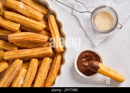 Churros mit Zucker und Schokolade auf hellem Hintergrund. Traditionelles spanisches Fast Food. Hausgemachtes Backen. Draufsicht Stockfoto