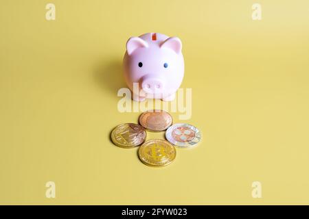 Sparschwein neben beliebten Krypto-Münzen auf gelbem Hintergrund. Bitcoin, Ripple XRP, Dogecoin und Ethereum. Investitionen, Sparen, Halten, Krypto kaufen Stockfoto