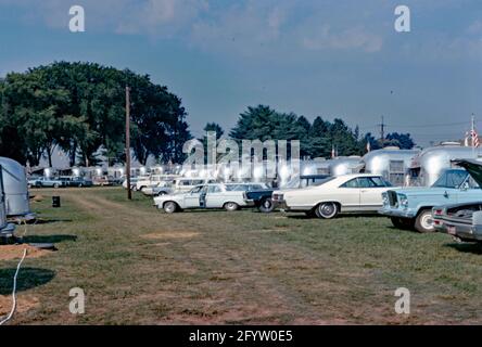 Eine Versammlung oder Kundgebung auf einem Campingplatz mit kultigen Airstream-Wohnwagen in den USA c. 1970. Der Airstream Caravan (Reiseanhänger) hat eine unverwechselbare abgerundete Form und eine Karosserie aus poliertem Aluminium. Diese Form stammt aus den 1930er Jahren und basiert auf dem Bowlus Road Chief, einem früheren Anhänger, der von Hawley Bowlus entworfen und gebaut wurde. Airstream-Anhänger und Freizeitfahrzeuge werden in Jackson Center, Ohio, USA, hergestellt. Dieses Bild stammt aus einer alten amerikanischen Kodak Amateur-Farbtransparenz – einem Vintage-Foto aus den 1960er/70er Jahren. Stockfoto