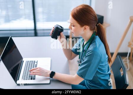 Seitenansicht einer seriöse Ärztin, die eine entfernte Online-Konsultation abgibt Zum Patienten über Laptop-Computer und trinken Kaffee aus der Tasse Stockfoto