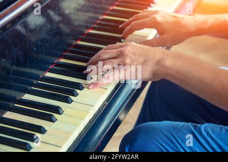 Ein Mann spielt ein altes Klavier. Männliche Hände auf den Tasten eines Vintage-Flügels Stockfoto