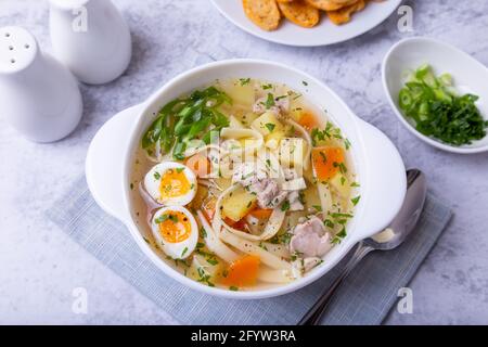 Suppe mit Hühnchen, Nudeln, Kartoffeln, Wachteleiern und Karotten. Gewürzt mit Zwiebeln und Petersilie. Nahaufnahme. Stockfoto