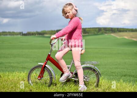 Mädchen in rosa Kleidung reitet ein Fahrrad auf dem Feld. Stockfoto