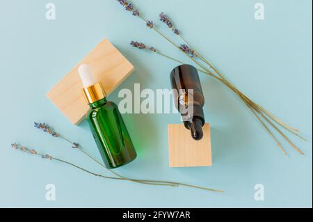 Ätherisches Öl mit einem Tropf und Lavendelzweigen auf blauem Hintergrund mit Holzwürfeln. Braune und grüne Glas Kosmetikflasche, Serum Stockfoto