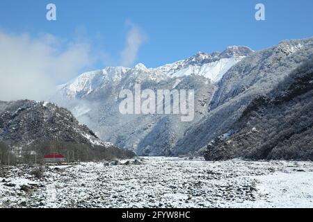 Flussbrücke. Winter und Berge . Es gibt Nebel am Fuße der Berge. Es schneite auf den Flusssteinen. Im Winter sank das Flusswasser Stockfoto