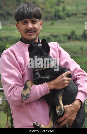 Vorderansicht eines hübschen jungen Mannes, der draußen mit steht Hält einen schwarzen Hund in den Händen Stockfoto