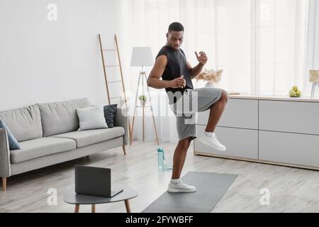 African Guy Tun Stehende Knie Erhöhen Übung Bei Laptop Indoor Stockfoto