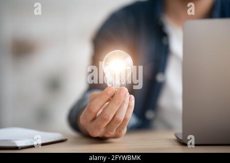 Nicht erkennbarer Mann mit beleuchteter Glühbirne, der im Büro sitzt Stockfoto