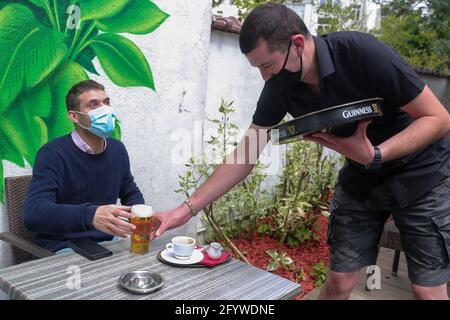 (210530) -- BRÜSSEL, 30. Mai 2021 (Xinhua) -- Luke Nolan (R) serviert einen Kunden mit einem Glas Bier in der Bar 'Funky Monkey', in Brüssel, Belgien, am 28. Mai 2021. Für Barmanager Luke Nolan kam die Entscheidung der belgischen Regierung, dem Gastgewerbe ab Mai 8 die Freiluftterrasse wieder zu eröffnen, nicht zu früh. Zuvor überlebten Luke und seine Kollegen Monate der harten Handhabung der Bar aufgrund der COVID-19-Pandemie und erspiesten abends Mahlzeiten zum Mitnehmen. „Es war eine große Erleichterung für alle und ausgezeichnet für uns, wieder an der Arbeit zu sein und hervorragend für unser mentales h Stockfoto