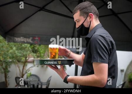 (210530) -- BRÜSSEL, 30. Mai 2021 (Xinhua) -- Luke Nolan serviert einen Kunden mit einem Glas Bier in der Bar 'Funky Monkey', in Brüssel, Belgien, am 28. Mai 2021. Für Barmanager Luke Nolan kam die Entscheidung der belgischen Regierung, dem Gastgewerbe ab Mai 8 die Freiluftterrasse wieder zu eröffnen, nicht zu früh. Zuvor überlebten Luke und seine Kollegen Monate der harten Handhabung der Bar aufgrund der COVID-19-Pandemie und erspiesten abends Mahlzeiten zum Mitnehmen. „Es war eine große Erleichterung für alle und ausgezeichnet für uns, wieder an der Arbeit zu sein und hervorragend für unsere geistige Gesundheit Stockfoto