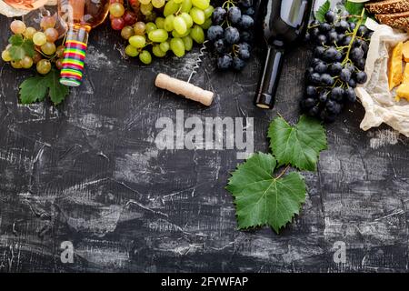 Rosé-Rotwein in Flaschen Käse, weiße rosa und schwarze Trauben mit Weinrebe Pflanze auf dunklem Beton Hintergrund. Sortiment verschiedene Arten von Wein und Trauben Stockfoto