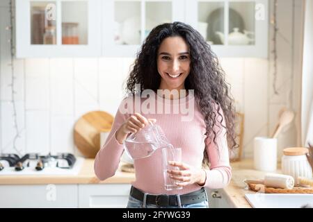 Gesunde Flüssigkeit. Porträt Einer Jungen Frau, Die Zu Hause In Der Küche Wasser Trinkt Stockfoto