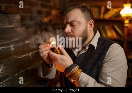 Bärtiger Mann zündet mit einem Streichholz eine Pfeife an Stockfoto