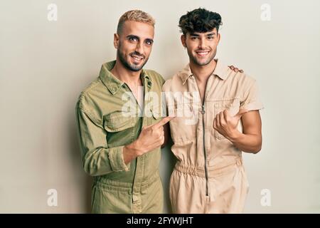 Homosexuell Gay paar stehen zusammen tragen lässig Jumpsuit fröhlich mit Ein Lächeln auf dem Gesicht zeigt mit der Hand und dem Finger nach oben Auf die Seite mit glücklich Stockfoto