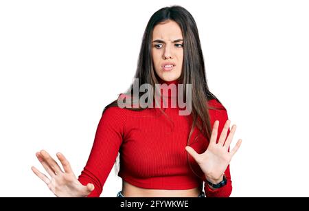 Junge Brünette Teenager trägt roten Rollkragenpullover angewiderten Ausdruck, unzufrieden und ängstlich tun Ekel Gesicht, weil Abneigung Reaktion. Stockfoto