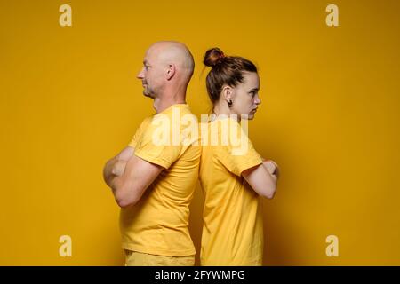 Verärgert stehen Mann und Frau mit gekreuzten Armen, Rücken zueinander, sie sind beleidigt und streiten sich. Gelber Hintergrund. Stockfoto