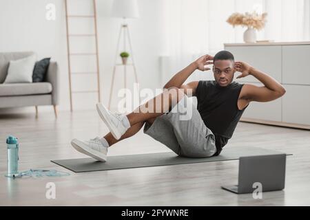 African American Guy Tut Ellenbogen-Knie-Bauch Crunches Auf Laptop Indoor Stockfoto
