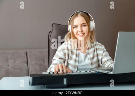 Eine Frau mit Kopfhörern lernt online mit einem Laptop in der Inneneinrichtung Klavier zu spielen. Frau spielen Synthesizer Klavier während Online-Unterricht mit teacher.Teenager Stockfoto