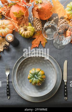 Herbst- und Thanksgiving-Tagestisch mit leerem Teller als Mockup verzierte Blätter, Kürbisse, stilvoller grauer Teller und Tischdecke. Draufsicht. V Stockfoto