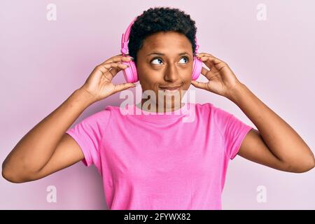 Junge afroamerikanische Mädchen, die Musik mit Kopfhörern hört, lächelt zur Seite und starrt weg denkend. Stockfoto