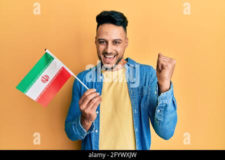 Junger araber, der die iranische Flagge hält und stolz schreit und mit erhobenem Arm den Sieg und den Erfolg feiert Stockfoto