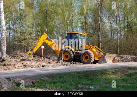 Ein Traktor mit Eimer gräbt ein Loch im Wald. Stockfoto