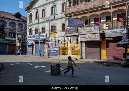 Srinagar, Indien. Mai 2021. Ein Junge spielt Cricket auf einer verlassenen Straße während einer Sperre, die verhängt wurde, um die Ausbreitung des Coronavirus in Srinagar zu verhindern. Die Regierung hat am Sonntag eine Lockerung der Lockdown-Richtlinien in Jammu und Kaschmir vom Montag an angeordnet, während die Bildungseinrichtungen bis zum 15. Juni geschlossen bleiben sollen. Indes verzeichnete Indien einen Tagesanstieg von 165,553 neuen COVID-19-Fällen, der niedrigste seit 46 Tagen mit 3,460 Todesfällen in den letzten 24 Stunden. Kredit: SOPA Images Limited/Alamy Live Nachrichten Stockfoto