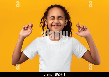 Hoffnungsvolles afroamerikanisches Mädchen, das ihre Finger kreuzt und Wunsch macht Stockfoto