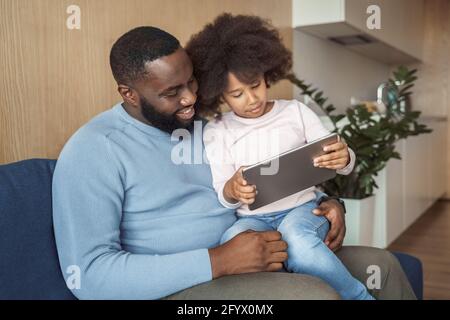 Lächelnder Vater und Tochter sitzen auf der Couch mit digitalem Tablet Zu Hause Stockfoto