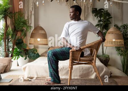 Sportlicher junger afrikanischer Mann, der mit einem Stuhl Yoga praktiziert, Drehstuhl-Pose macht, Parivrtta Utkatasana Stockfoto