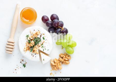 Brie- oder Camembert-Käse, serviert mit Trauben, Honig und Walnüssen auf einem Marmortisch, Draufsicht, Kopierraum Stockfoto