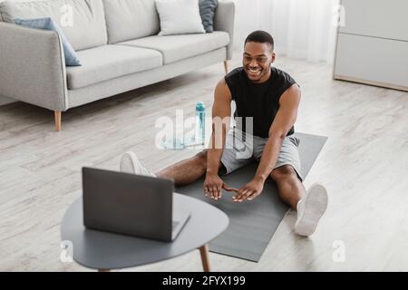 Happy African Man Tut Stretching-Übung Bei Laptop Zu Hause Stockfoto