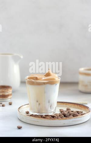 Iced Dalgona Kaffee mit flauschigen süßen Schaum in einem Glas auf einem grauen Hintergrund. Trendigen Sommergetränk. Vertikales Bild. Raum kopieren. Stockfoto